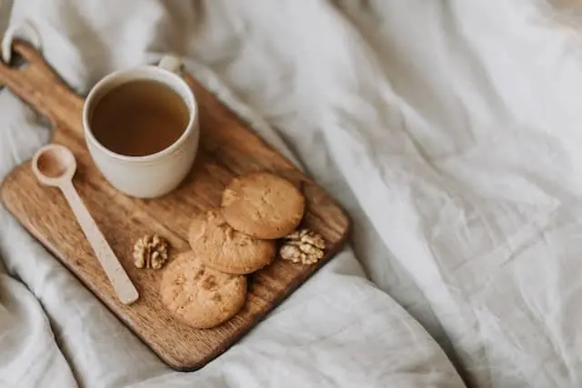 담요위에 나무도마가 있고 도마위에 쿠키와 차 한잔이 있는 모습